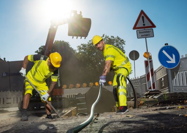 Two road construction workers are working in work clothes with UV protection in hot weather.