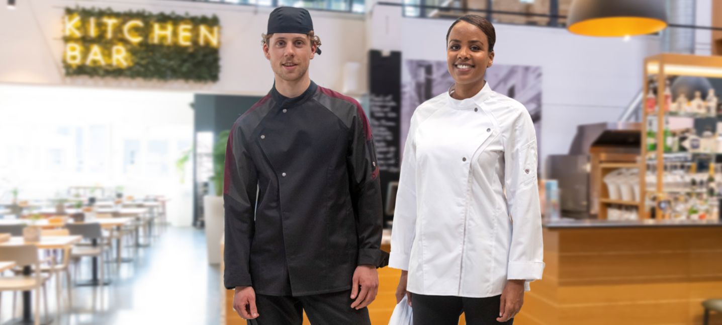 A woman and a man wearing chef's jackets and headbands are standing in a kitchen.