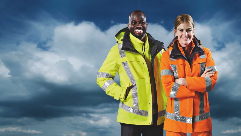 Two people in weatherproof high-visibility clothing against a dark sky, one in yellow, one in orange.