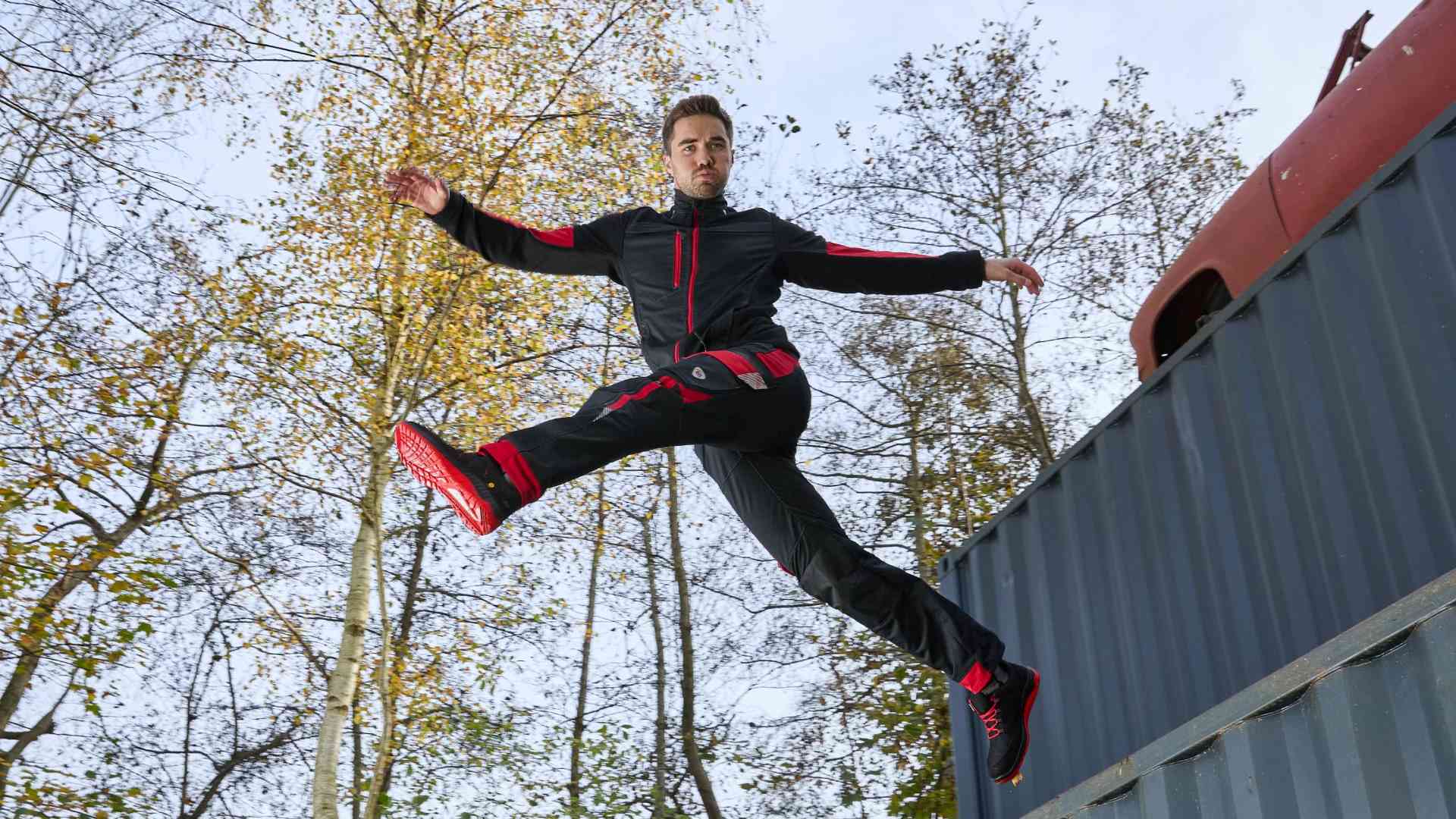 A man jumps from a container with his legs apart, wearing 幸运飞行艇168体彩开奖网® work clothes.