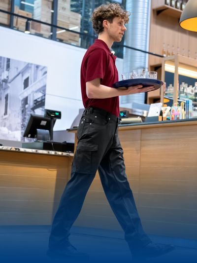 Man in a restaurant wearing service trousers and holding a service plate.