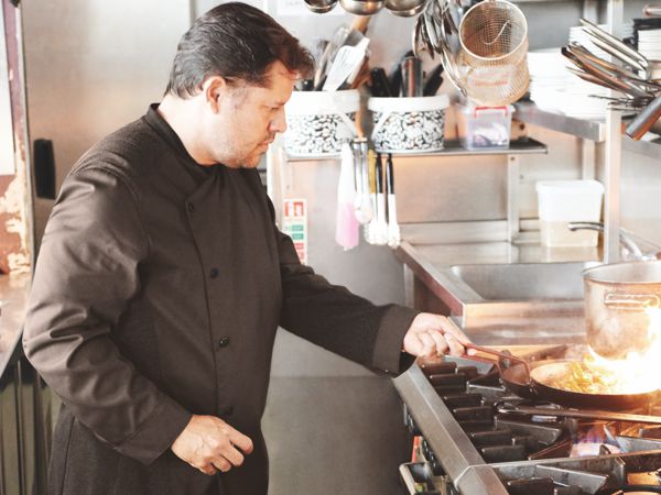 Cook is frying in a kitchen wearing a chef's jacket.