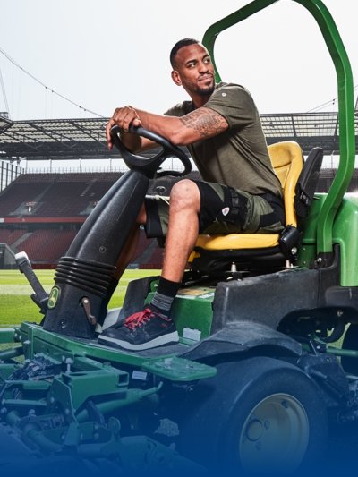 A greenkeeper in work clothes mows the grass at the Rheinenergiestadion.