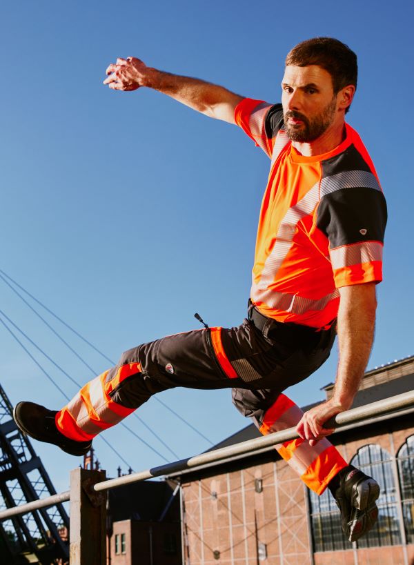 A man in hivi's orange work clothes jumps over a pole.