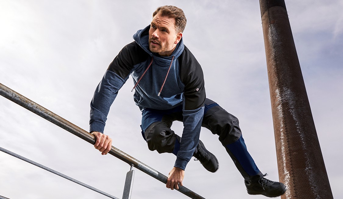 A man in hybrid and flexible work trousers jumps over a pole.