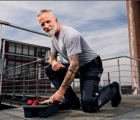 Man in kneeling position reaches into toolbox and wears super stretch work trousers.