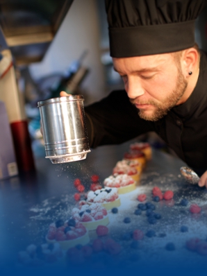 Pastry chef tipping icing sugar and wearing chef's clothes.