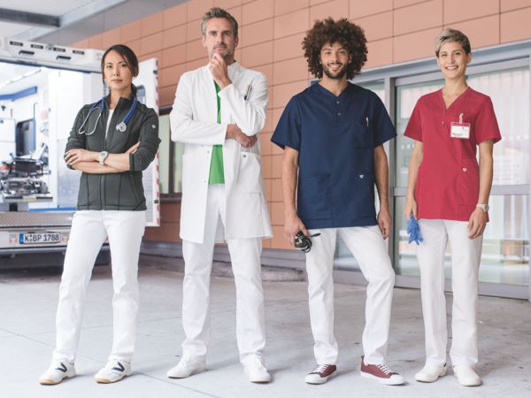 Two women and two men pose in front of a hospital in different hospital uniforms.