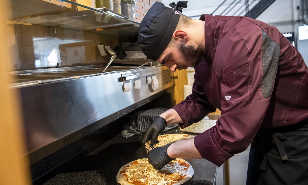 A pizza chef wears black headgear and bordeaux chef's clothing.