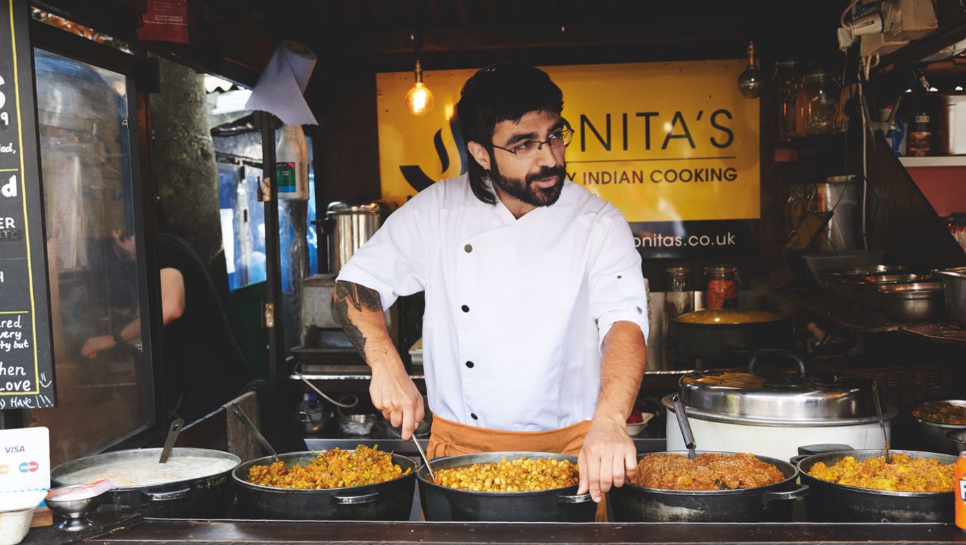 A male street food chef wears a white chef's jacket in his food truck.
