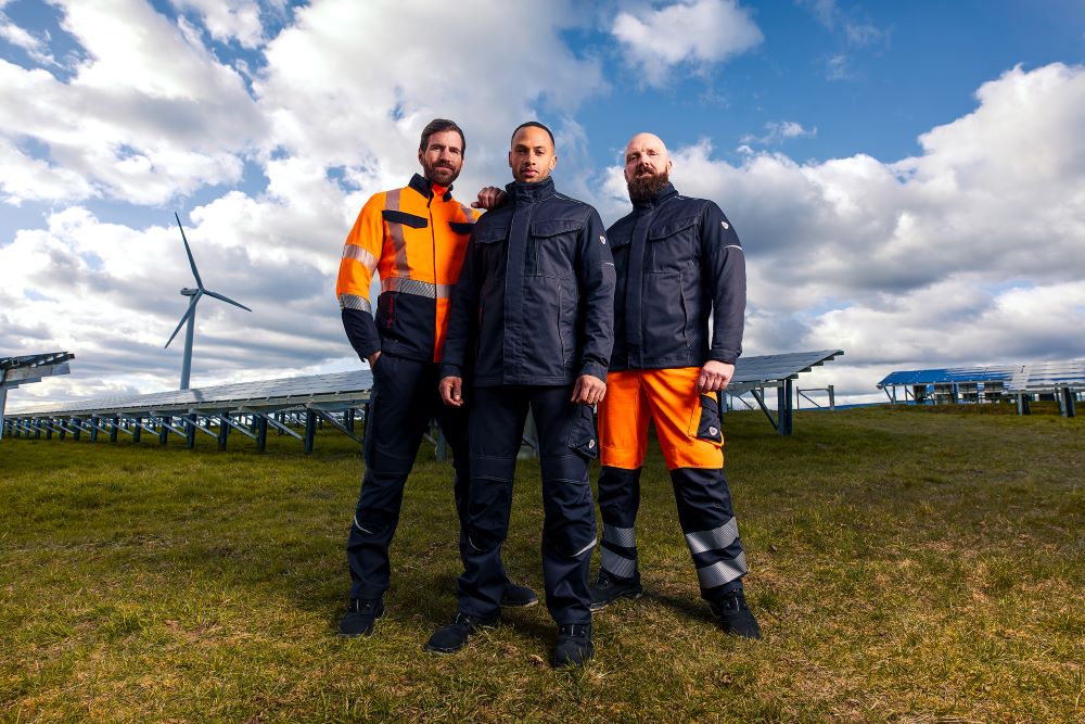 Three people in modern work clothes in front of solar and wind turbines.