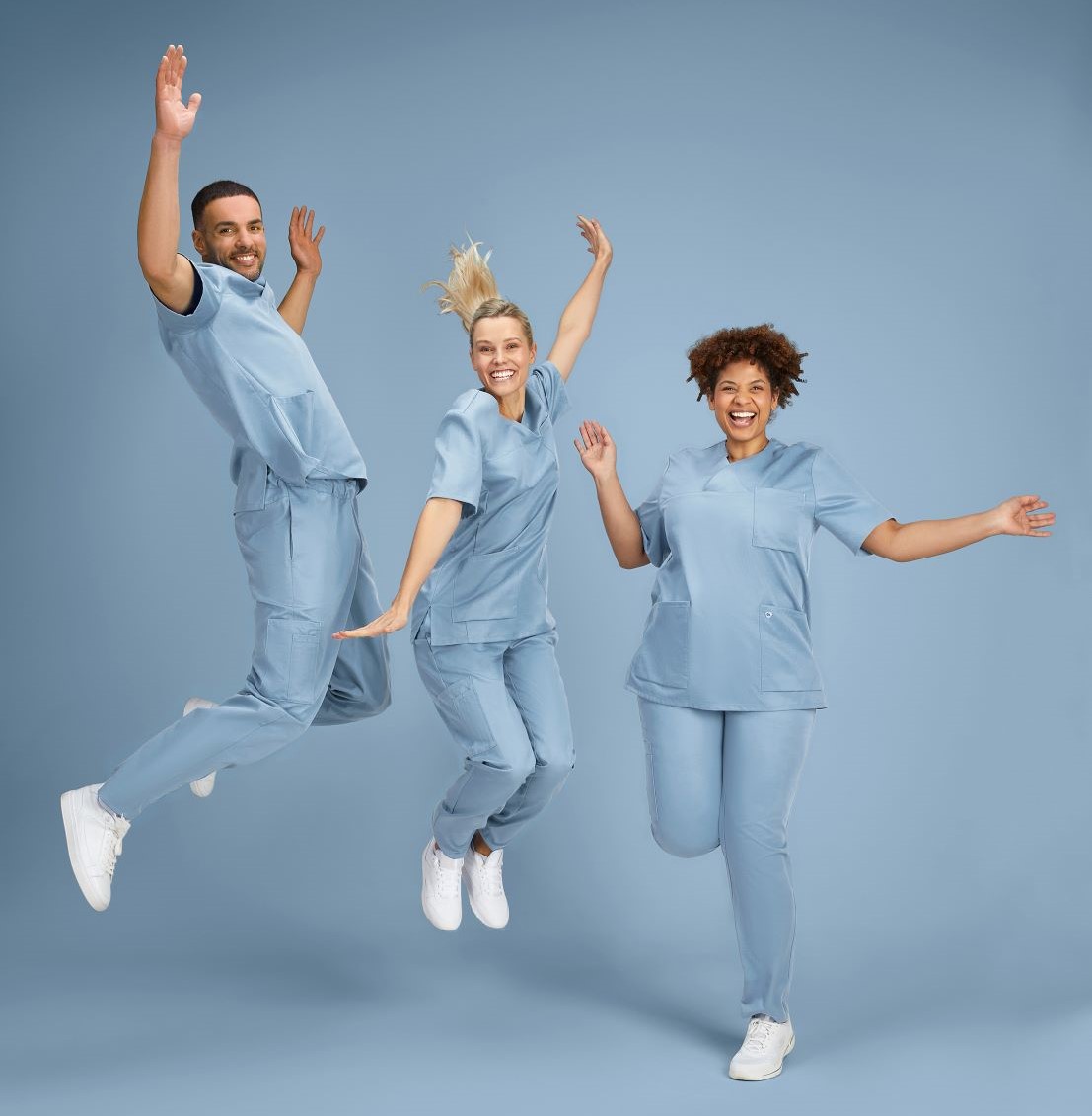 A man and two women in light blue Tencel medical outfits jump in the air.