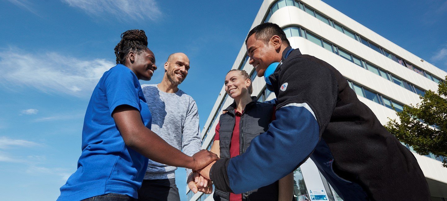 A team puts their hands on each other in workwear clothing.
